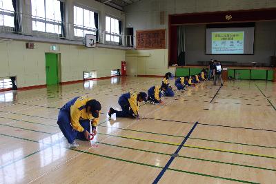 体育館に区割りのテープを貼る少年消防団員